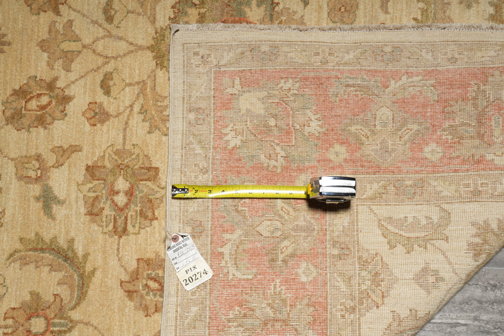 A square area rug with a faded pink and beige floral pattern is shown on a wood floor next to a matching floral area rug, with a tape measure and price tag laid across the corner.
