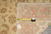 Load image into Gallery viewer, A square area rug with a faded pink and beige floral pattern is shown on a wood floor next to a matching floral area rug, with a tape measure and price tag laid across the corner.
