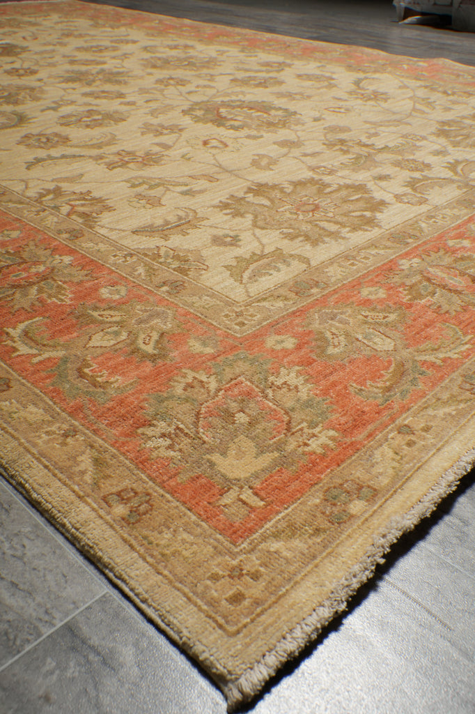 A traditional oriental-style area rug with a beige center and a rust-red border, laid out on a gray tiled floor.