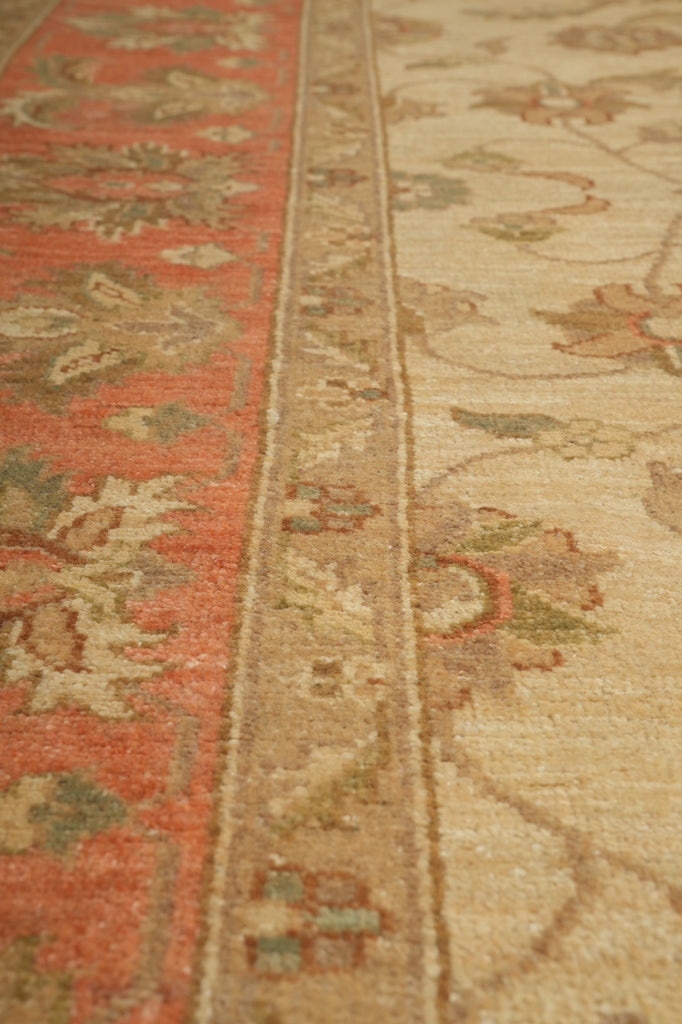 Close-up of a patterned area rug showing a rust red upper border, a beige central band, and a cream lower section with floral motifs.