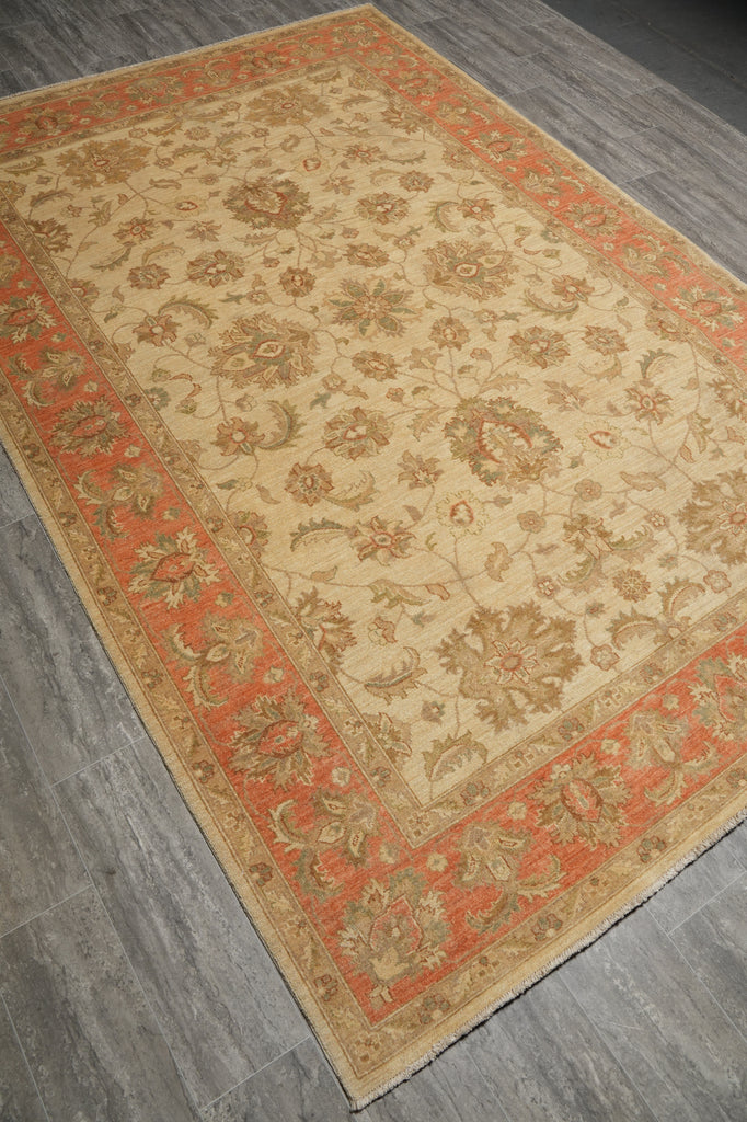 A rectangular area rug with an intricate floral pattern, featuring a beige center field and a rust-orange border, shown on a gray wood-look floor.