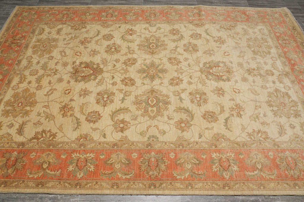 A rectangular area rug with an ornate floral and vine pattern, featuring a warm beige center field and rust-orange borders.