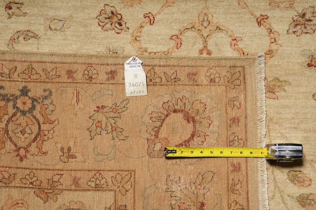 A close-up of a patterned area rug in beige and rust tones, with a yellow tape measure laid across the border and a white tag attached near the edge.