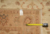 Load image into Gallery viewer, A close-up of a patterned area rug in beige and rust tones, with a yellow tape measure laid across the border and a white tag attached near the edge.