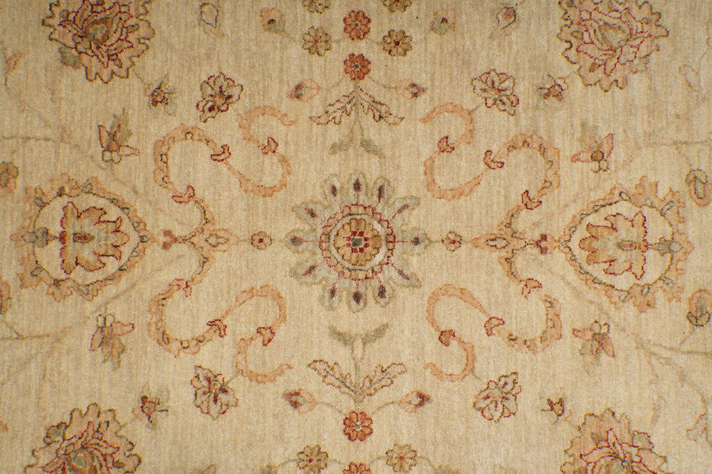 A close-up of a traditional patterned rug with a central floral medallion and symmetrical scrollwork in muted beige, rust, and dusty pink tones.