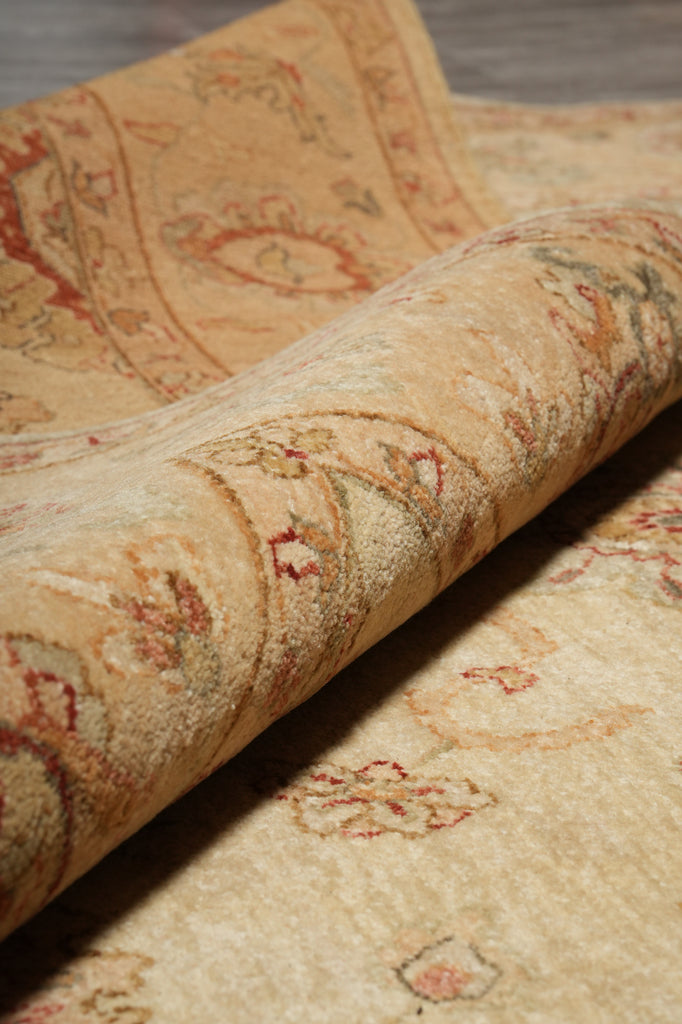 A close-up of a rolled area rug showing its detailed beige and cream pattern with red and green accents.