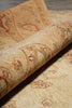 Load image into Gallery viewer, A close-up of a rolled area rug showing its detailed beige and cream pattern with red and green accents.