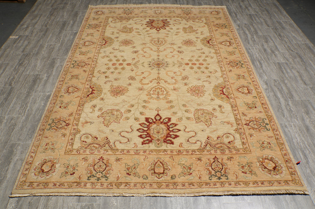 A rectangular traditional area rug with an intricate floral and medallion pattern, laid out on a gray wood-plank floor. The rug features a warm beige base with red, green, and brown accents.
