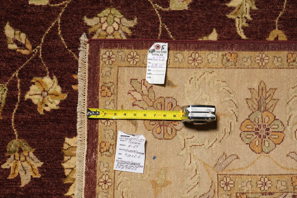 A folded area rug with a floral pattern in beige, brown, and gold tones, shown with a yellow tape measure and two inventory tags on top to indicate size and condition.