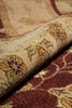 Load image into Gallery viewer, Close-up of a patterned area rug with a rolled section showing its texture and design. The rug features a traditional floral motif in burgundy, beige, ochre yellow, and olive green.