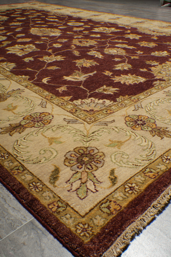 A close-up view of an oriental area rug with a traditional floral pattern, featuring a cream center, a dark brown field, and a decorative border, shown on a gray tiled floor.