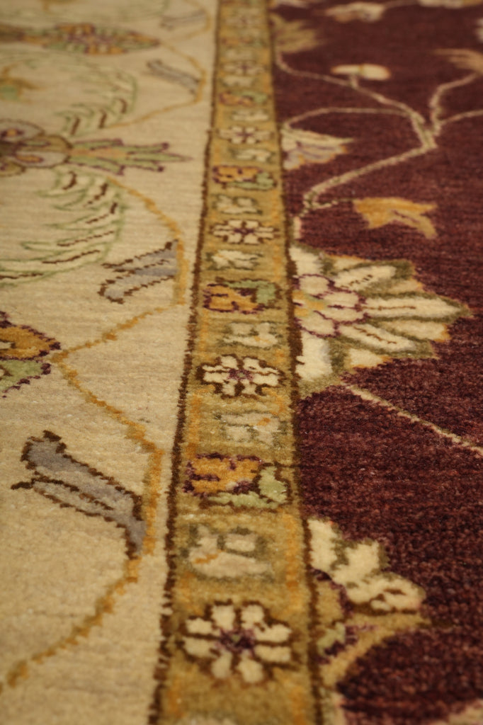 Close-up of a patterned rug showing a cream field with stylized animal motifs, a decorative beige border with floral and geometric motifs, and a deep burgundy lower section with large floral shapes.