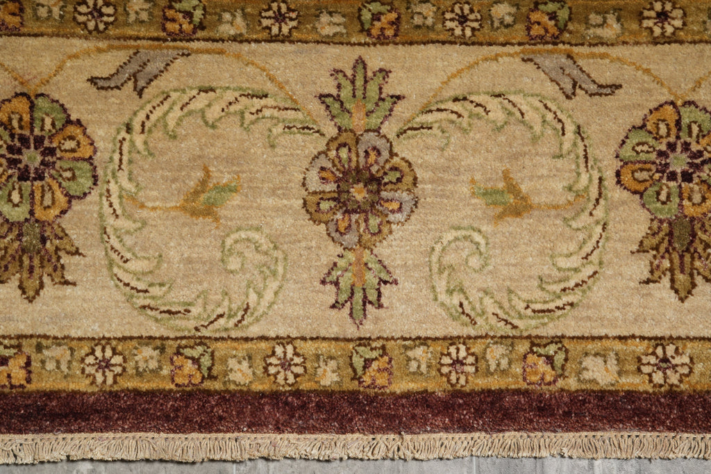 Close-up of a traditional patterned rug with a central floral medallion, scrolling motifs, floral corners, and a dark burgundy border with fringe.