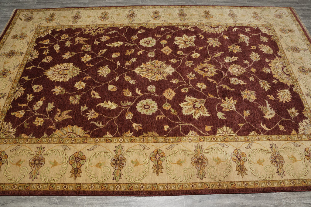 A rectangular area rug with a traditional floral pattern, featuring a deep burgundy center field and a beige border, laid out on a gray tiled floor.