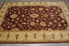 Load image into Gallery viewer, A rectangular area rug with a traditional floral pattern, featuring a deep burgundy center field and a beige border, laid out on a gray tiled floor.