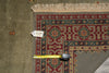 Load image into Gallery viewer, A close-up of a patterned area rug corner with fringe, shown on a neutral surface with a tape measure and price tag nearby.