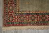 Load image into Gallery viewer, A close-up of a patterned area rug corner with a beige field, red and green geometric borders, and cream fringe along the bottom edge.