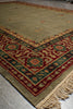 Load image into Gallery viewer, A close-up of a patterned area rug with a beige base, featuring a red, green, and orange geometric border and fringe on one end.