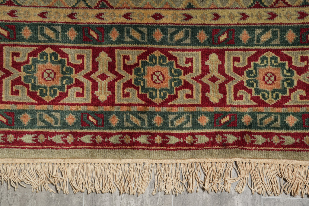 A close-up of a patterned area rug with a cream fringe, featuring red, teal, and beige geometric motifs.