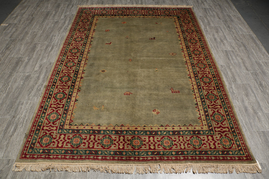 A rectangular area rug with a muted sage green center and a detailed multicolor border in red, beige, and green, shown on a gray wood-look floor.