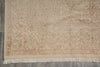 Load image into Gallery viewer, A close-up of a beige area rug with an intricate floral and botanical pattern and fringed edges, laid out on a gray floor.