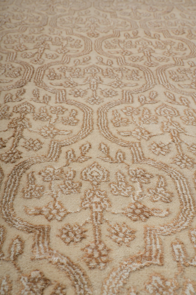 A close-up of a beige and tan patterned fabric or carpet texture with an ornate floral and scroll motif.