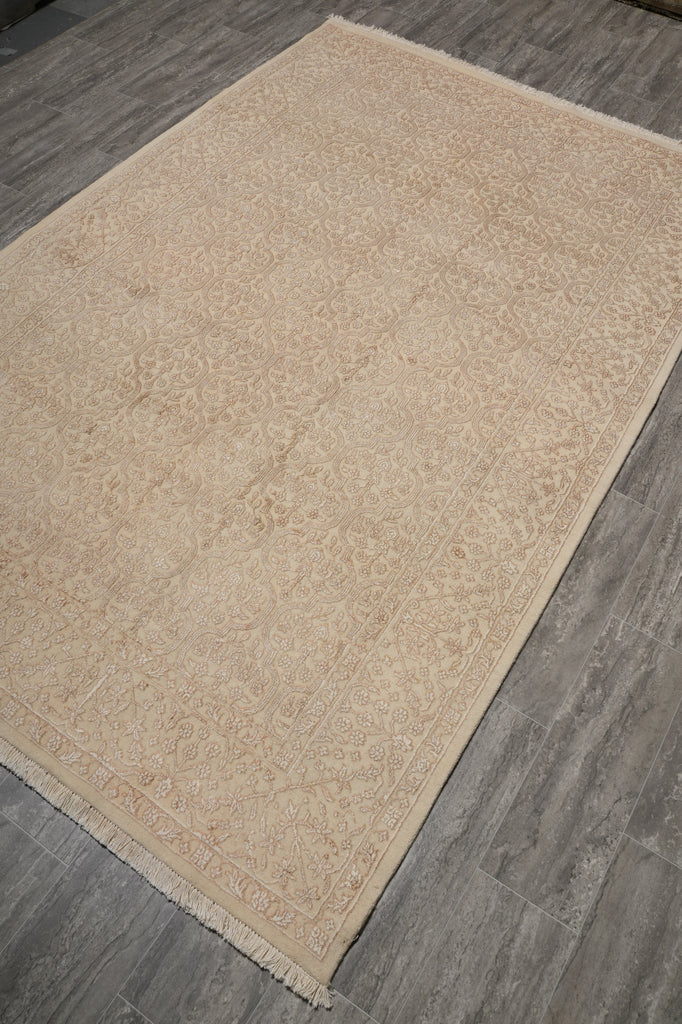 A rectangular area rug with a traditional floral pattern in beige and cream tones, laid out diagonally on a gray wood-look floor.