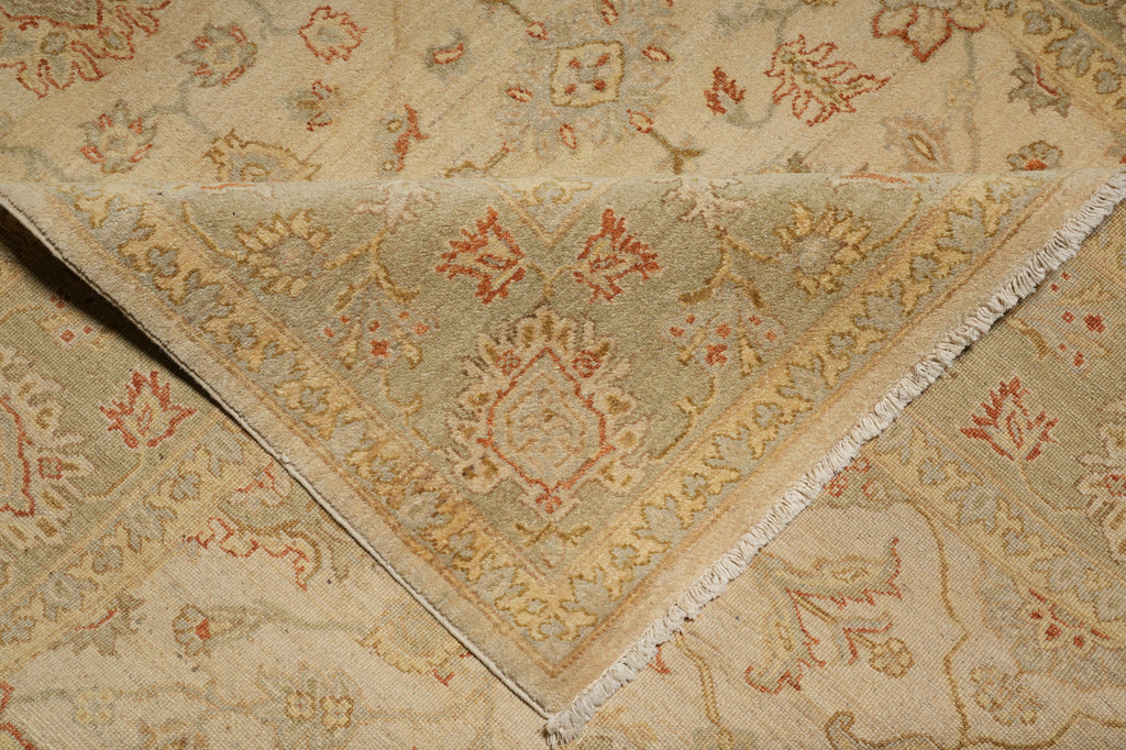 A close-up of a folded area rug showing its intricate traditional pattern in beige, muted green, and terracotta red.