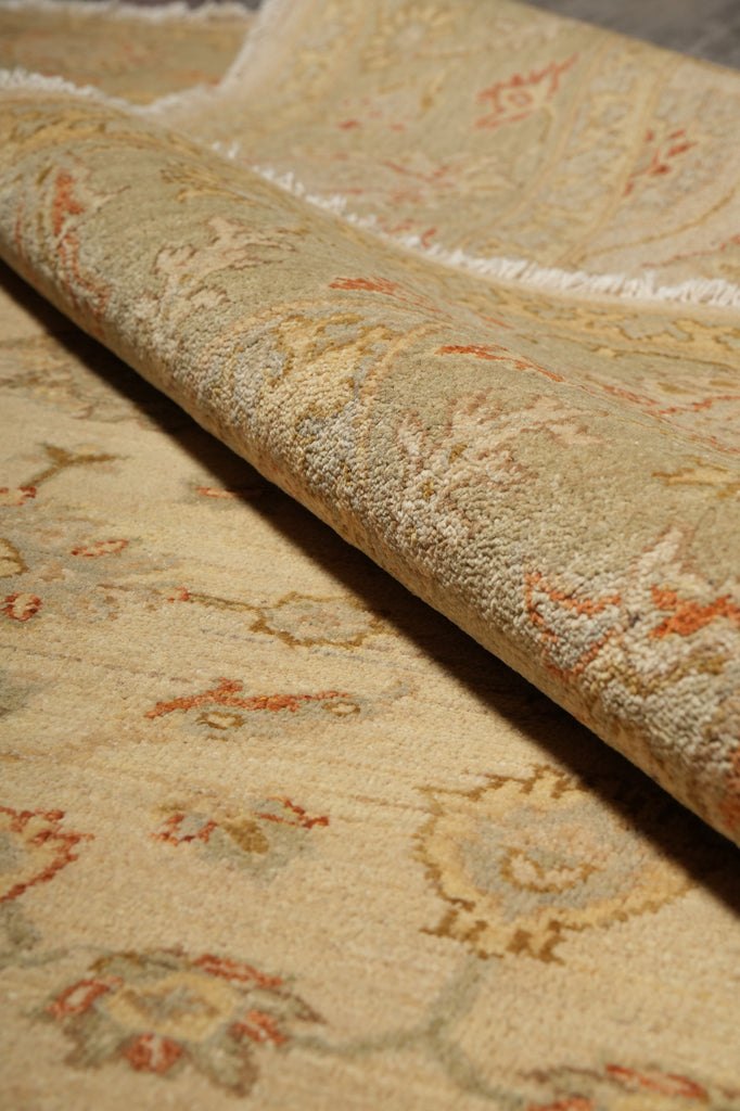 A close-up of a rolled area rug showing its detailed traditional floral pattern in beige, cream, and muted orange tones.