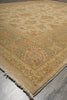 Load image into Gallery viewer, A close-up view of a traditional area rug with a beige and cream base, featuring a central medallion and ornate floral motifs in muted orange and brown, laid out on a gray floor.