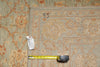 Load image into Gallery viewer, An overhead view of a patterned area rug with a tape measure and price tag placed on it for scale. The rug has a beige and gray base with orange-brown floral motifs and a black handwritten '95' on one corner.