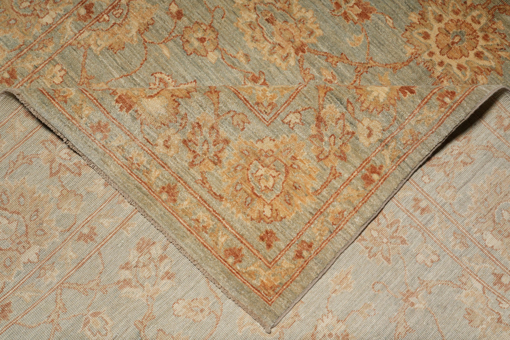 A close-up of a traditional patterned rug corner showing a dusty blue-gray field with warm beige and rust floral motifs and a matching border.