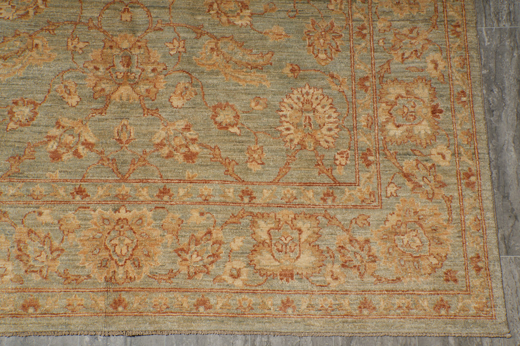 A close-up of a traditional patterned area rug with a muted sage green base, featuring warm beige and terracotta floral motifs and borders.