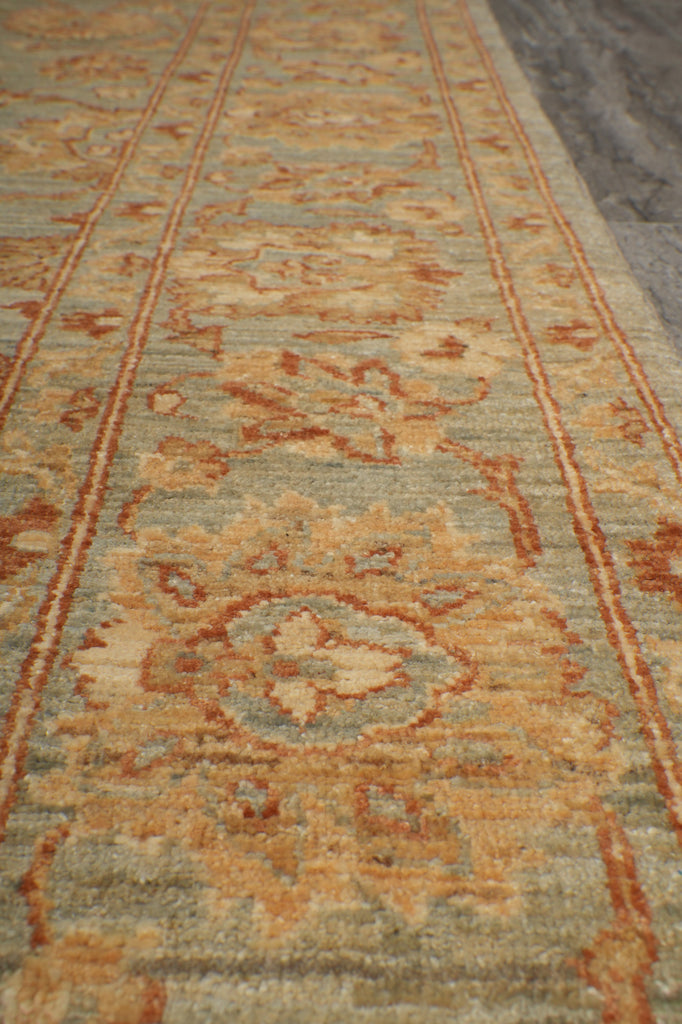 A close-up view of an area rug with a traditional floral pattern in muted tones of beige, rust orange, and pale sage green.