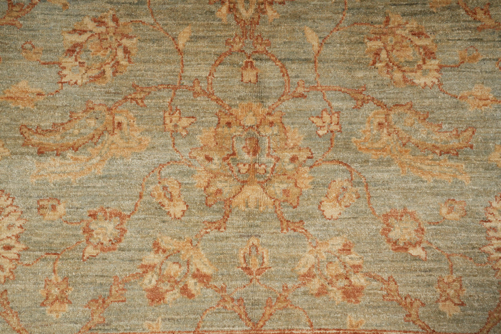 A close-up of a traditional patterned rug with a muted sage green background and warm beige and rust floral motifs.