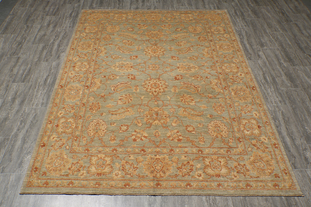 A rectangular area rug with an ornate floral and medallion pattern in muted sage green, tan, and rust orange, laid flat on a gray wood-look floor.