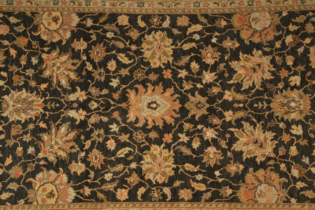 An ornate traditional area rug with a dark black background and intricate floral motifs in beige, gold, and muted orange, featuring a decorative border.