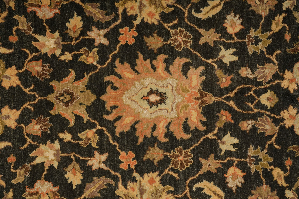 A close-up of a traditional patterned rug with a dark charcoal background and a central floral medallion in muted orange, beige, and brown tones.