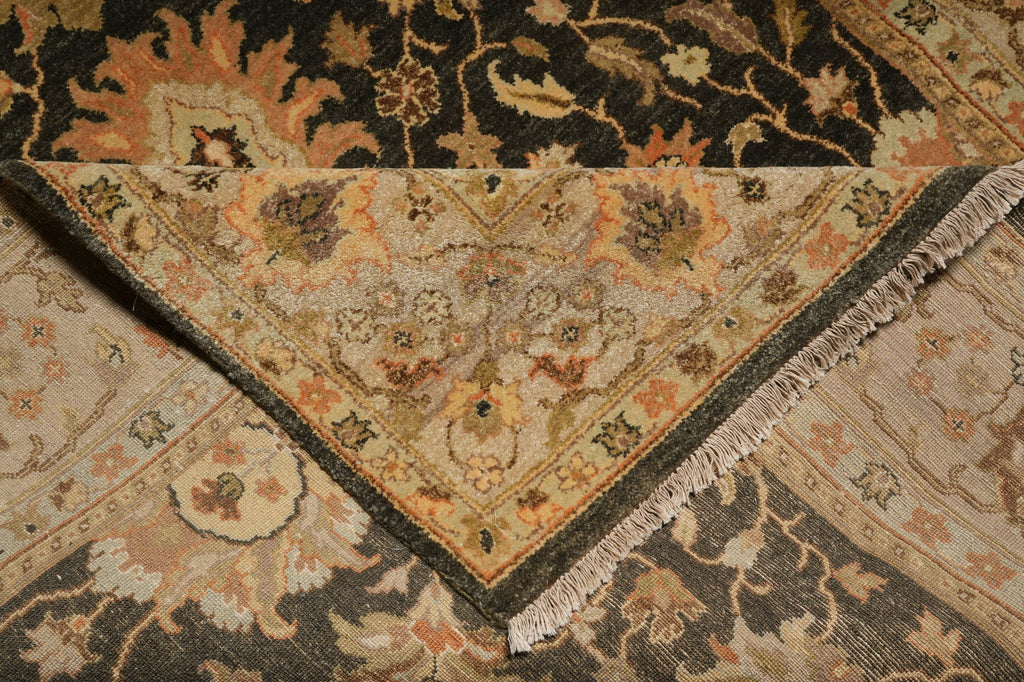 A close-up of a traditional patterned rug with a folded corner showing its beige and brown floral medallion design, dark gray border, and fringed edge.