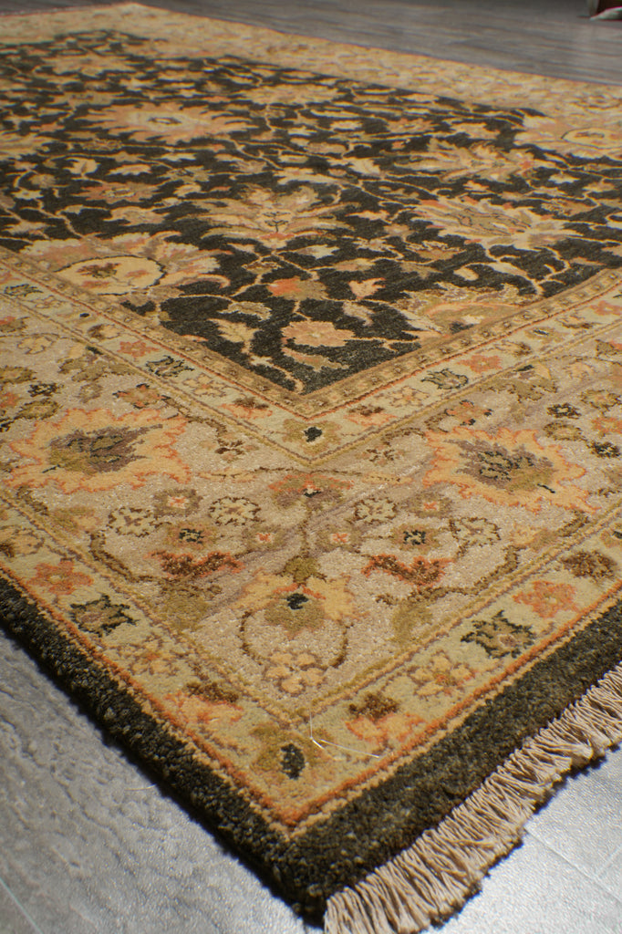 A traditional oriental area rug with an intricate floral and geometric pattern, shown laid out on a gray floor. The rug features a dark brown central field, a beige and orange border, and matching fringed edges.