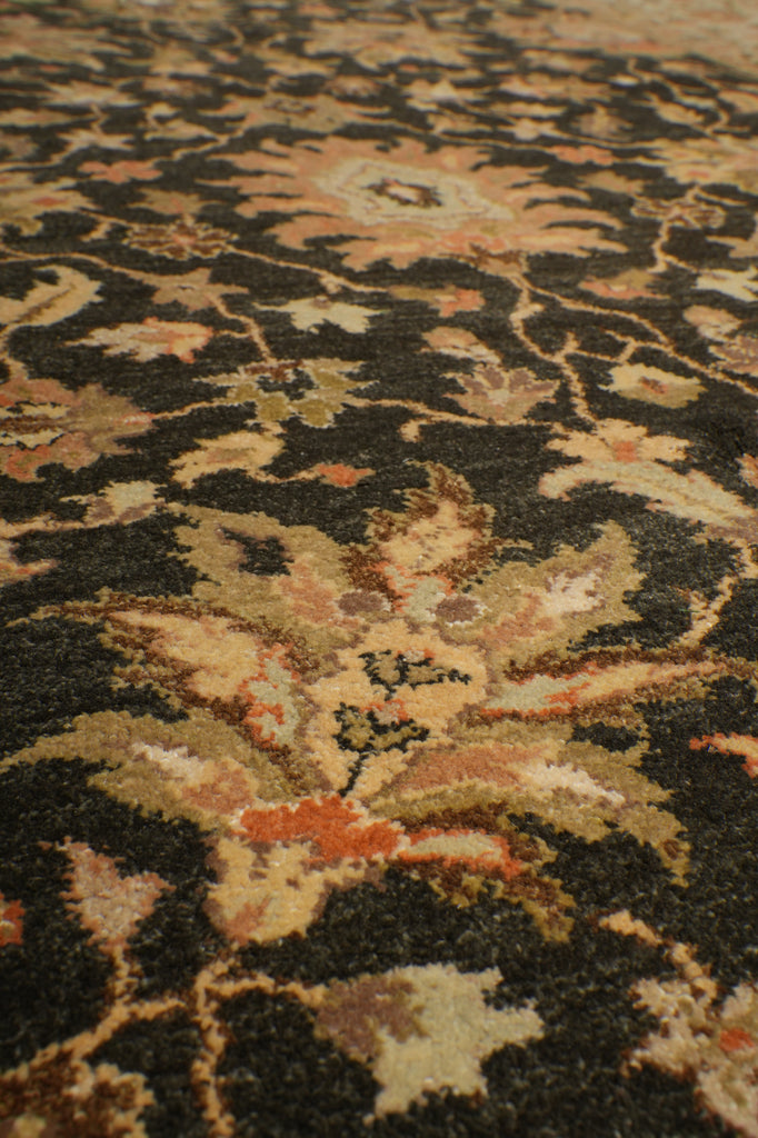 Close-up of an ornate patterned rug with a dark charcoal-black base and intricate floral motifs in beige, tan, muted orange, and brown.