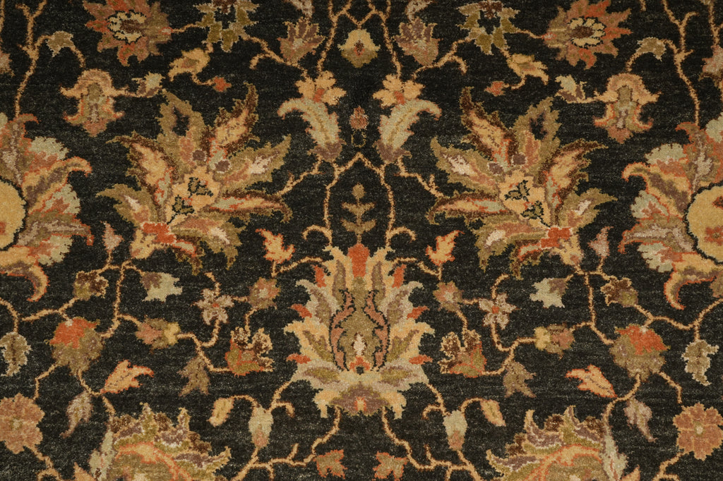 A close-up of a traditional patterned rug with a dark charcoal background and ornate floral motifs in beige, tan, muted orange, and brown.