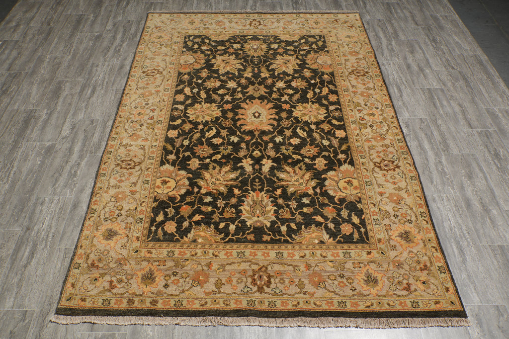 A rectangular area rug with a traditional floral pattern, featuring a dark central field surrounded by a wide beige and orange border, laid out on a gray wood-look floor.