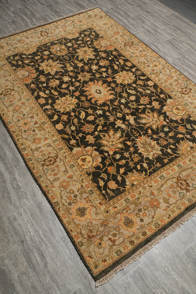 A rectangular area rug with a dark central field and ornate floral motifs, photographed at an angle on a gray wood-look floor.