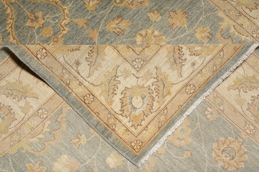 Close-up of a patterned area rug showing a folded corner that reveals the fringed edge, with a floral and medallion design in beige, tan, and muted blue-gray tones.