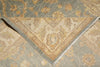 Load image into Gallery viewer, Close-up of a patterned area rug showing a folded corner that reveals the fringed edge, with a floral and medallion design in beige, tan, and muted blue-gray tones.