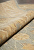 Load image into Gallery viewer, Close-up of a patterned rug or textile with a rolled section showing its texture and design. The color palette is a mix of beige, tan, gray, and muted blue-gray in a marbled or floral-inspired pattern.