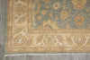 Load image into Gallery viewer, A close-up of a traditional patterned rug corner, showing a dusty blue field with beige and ochre floral motifs and a cream border, laid on a gray floor.