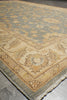 Load image into Gallery viewer, A close-up view of an area rug showing its corner detail, featuring a traditional floral pattern in beige, cream, and muted blue-gray tones with a fringed edge.