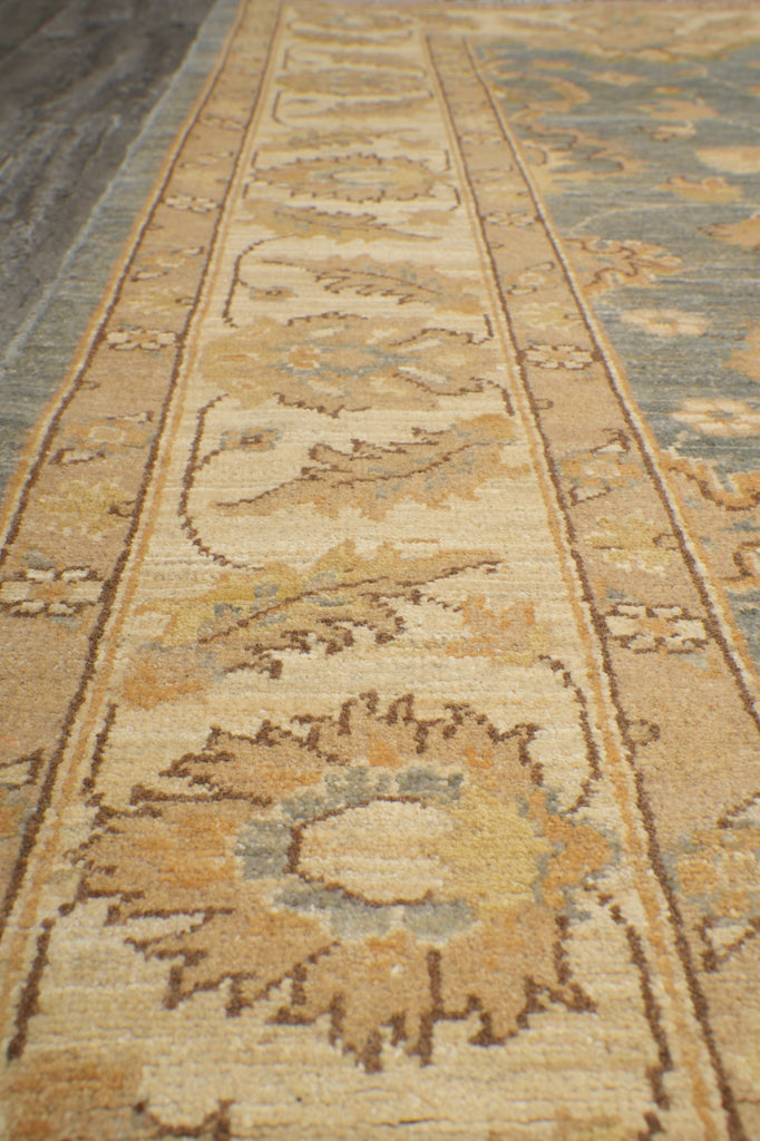 Close-up of an ornate patterned area rug with beige, tan, muted blue, and brown woven motifs.